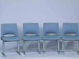 four blue chairs sitting in a row against a white wall