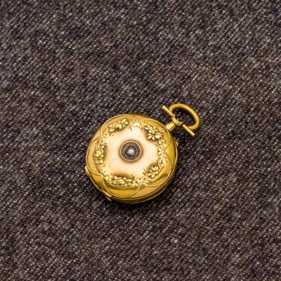 une petite montre de poche en or posée sur un tissu marron