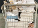 une cage métallique remplie d'une multitude de papiers, posée par terre