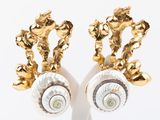 une paire de boucles d'oreilles en forme de coquillage, dorées et blanches, posées sur un socle blanc