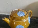 a yellow teapot with a blue flower on it