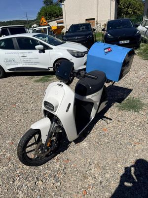un scooter blanc garé sur un parking, à côté d'autres voitures