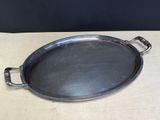 an oval metal tray with handles on a wooden table