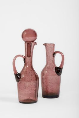 une paire de vases en verre rose posés sur une surface blanche, sur fond blanc