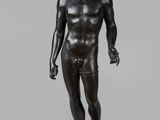 une statue en bronze représentant un homme debout sur un socle en bois
