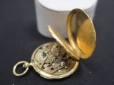 a gold pocket watch sitting on a table next to a white container