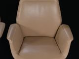 pair of tan leather office chairs on casteors against a black background