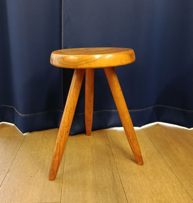 un petit tabouret en bois posé par terre devant un rideau