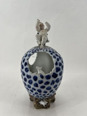 une petite figurine posée sur un vase bleu et blanc