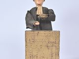 figurine of a man sitting on a podium with his hands clasped