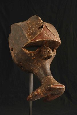 un masque en bois posé sur un socle, sur fond noir