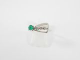 une bague en forme de nœud, sertie d'une émeraude et de diamants, sur fond blanc