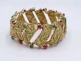 a close up of a gold bracelet with green and red stones