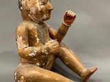 an old wooden figurine of a man sitting on the ground holding a piece of wood