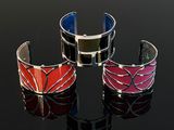 three different colored cuff bracelets on a black surface