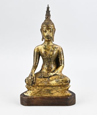 une statue en or représentant un Bouddha assis, posée sur un socle en bois