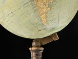 an old world globe on a wooden stand against a black background