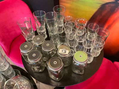 many glasses and jars on a table with a pink chair in the background