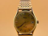 une image représentant une montre-bracelet en or posée sur un socle, sur fond jaune
