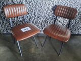 two brown leather chairs sitting next to each other in front of a wall