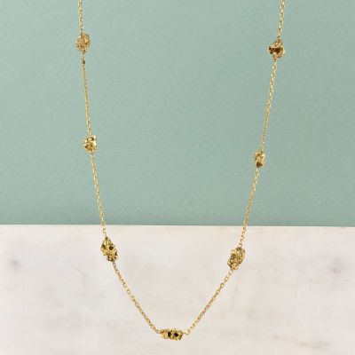 un collier plaqué or orné de quatre petites perles, posé sur une surface en marbre