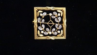 un gros plan d'une broche en or et diamants posée sur une surface noire