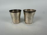 two silver cups with designs on them sitting on a white surface