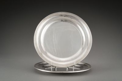 une assiette en argent posée sur un support à assiette en argent, sur un fond gris