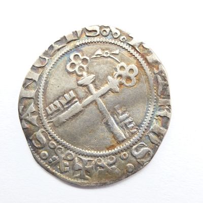 une vieille pièce d'argent ornée d'une croix, posée sur une surface blanche