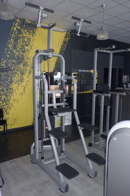 une salle de sport équipée d'appareils et dont l'un des murs est jaune et noir