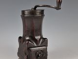 un moulin à café ancien muni d'un manche en bois, sur fond gris