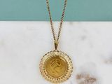 une photo d'un collier avec une pièce d'or posé sur une surface en marbre