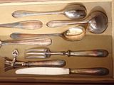 a lot of silver spoons and spoon knives in a box