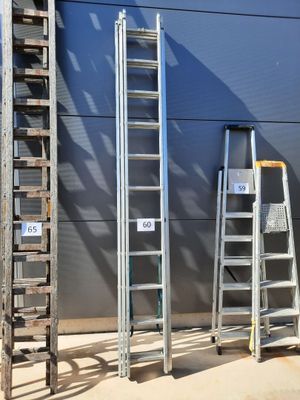 Plusieurs échelles sont alignées contre un mur devant un immeuble.