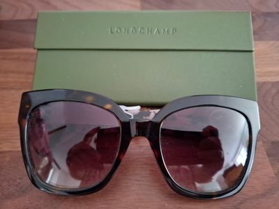 Quelqu'un tient une paire de lunettes de soleil posée sur une table en bois.