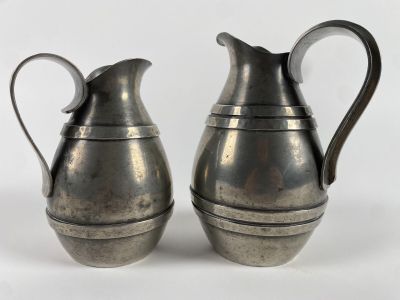 two silver pitchers sitting next to each other on a white surface