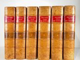 six old books are lined up in a row on a white surface