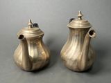 two silver teapots sitting next to each other on a table