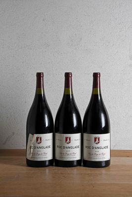 three bottles of wine sit on a wooden table in front of a wall