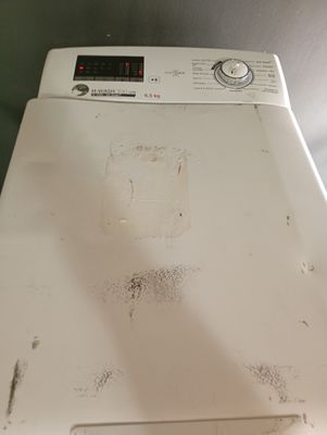 une machine à laver sale posée sur une machine à laver blanche