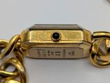 a gold watch with a chain around it on a white surface