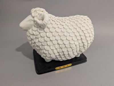 un mouton blanc posé sur un socle noir