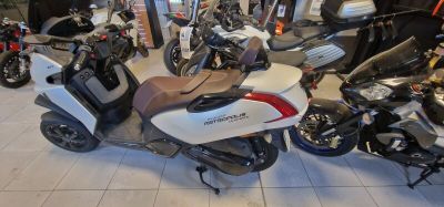 Plusieurs motos sont garées dans un showroom, autour desquelles se trouvent des personnes.