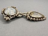 two pieces of silver jewelry on a table with a gray background