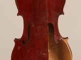 Un vieux violon est posé sur un chevalet, sur une surface blanche.