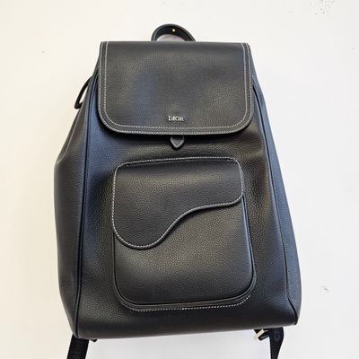 sac à dos en cuir noir à roulettes posé sur une surface blanche, sur fond blanc