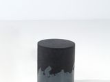 un vase noir posé sur une table blanche, près d'un mur blanc