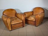 two brown leather chairs sitting next to each other on a tiled floor