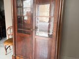 une armoire en bois avec des portes vitrées, devant laquelle se trouve une chaise