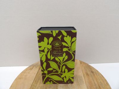 une boîte verte et une autre marron posées sur une table en bois devant un mur blanc